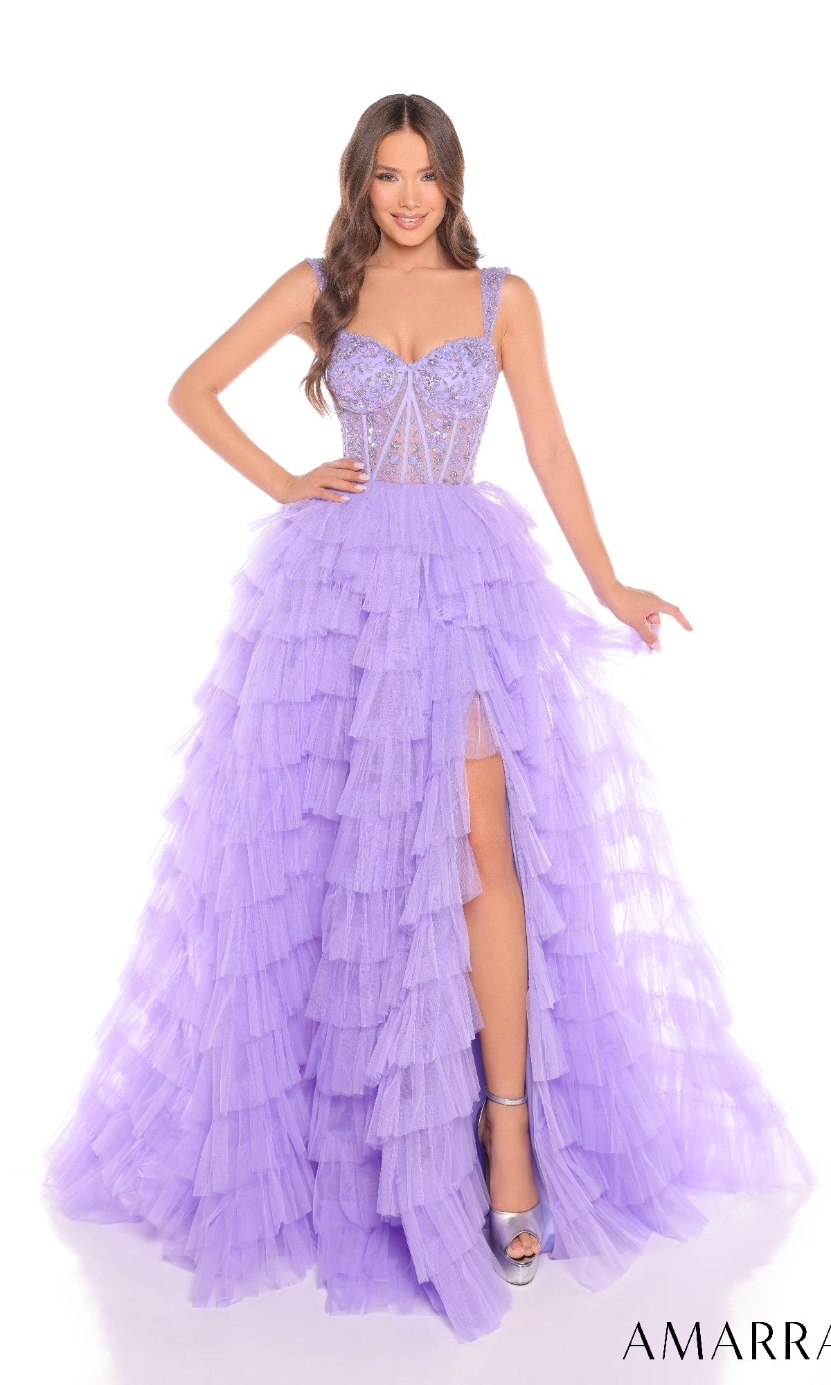 A woman smiles at the camera in the Amarra 88388 long prom dress, featuring an A-line silhouette with a layered lavender ruffle tulle skirt, structured bodice, sheer panels, thigh-high slit, and metallic heels.